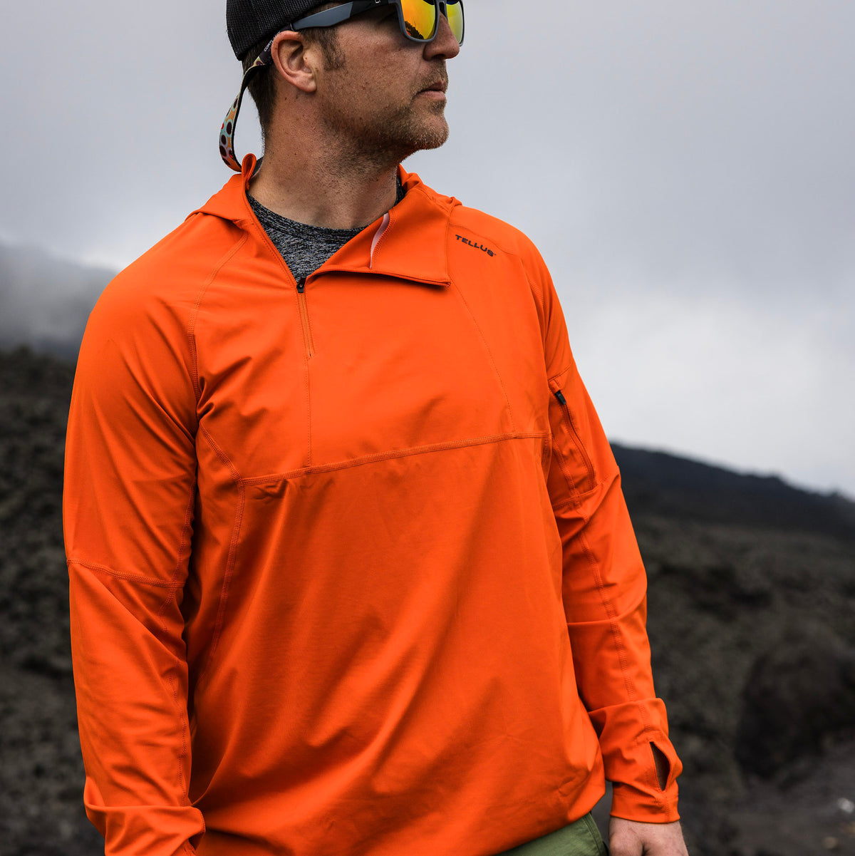 Man wearing orange Satanka Cove Hoodie looking off to the right on a hilltop with misty, cloudy background