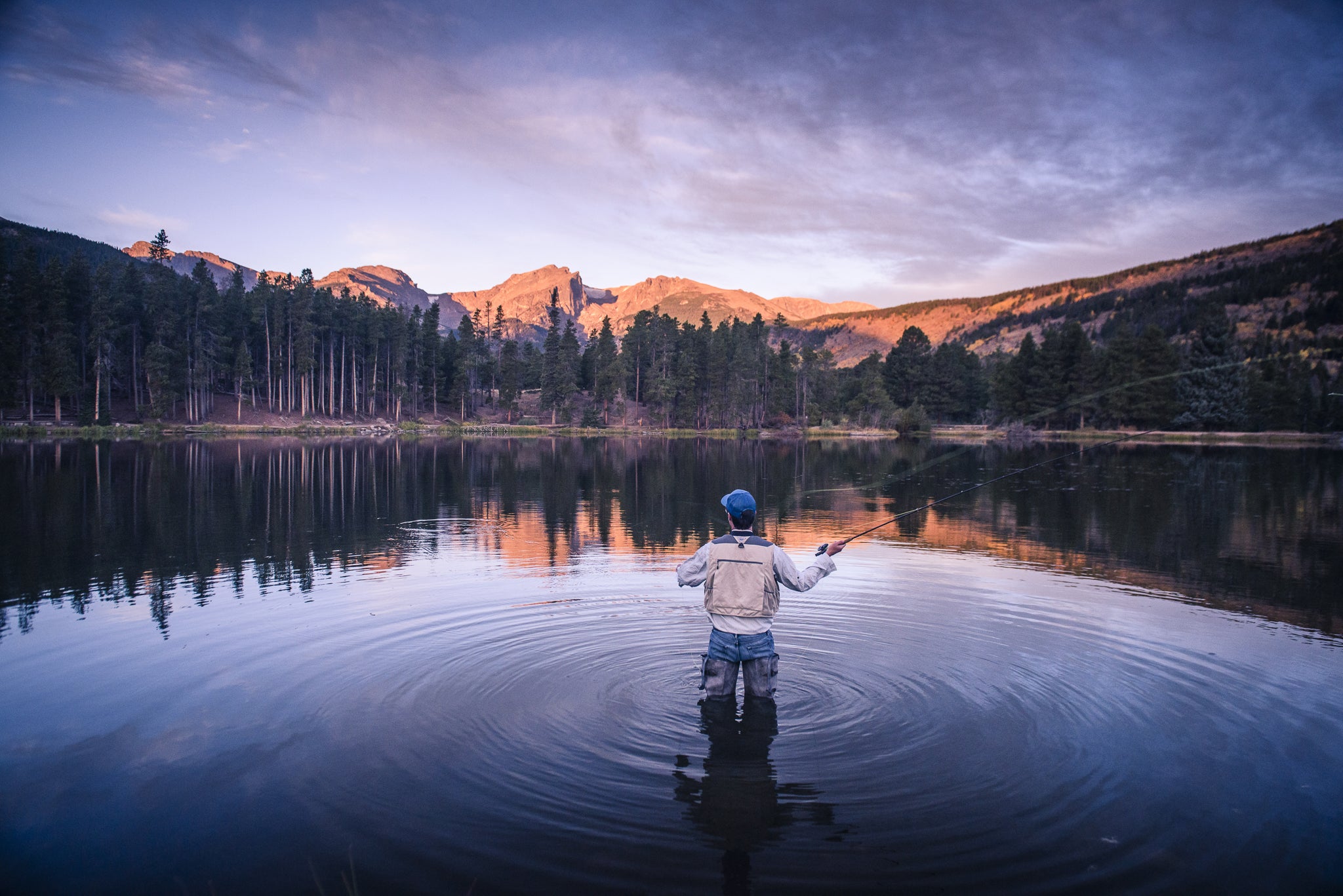Person fishing in a lake with mountains and trees in the background