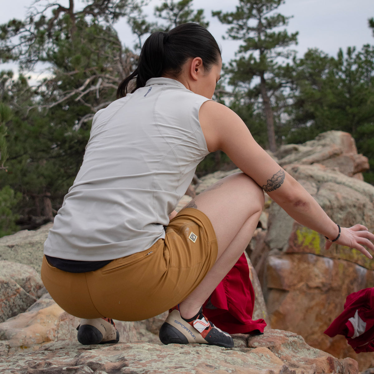 Woman crouching wearing gray Satanka Cove Tank and bistre Trail Ridge Trek Shorts showing back of tank and back of shorts