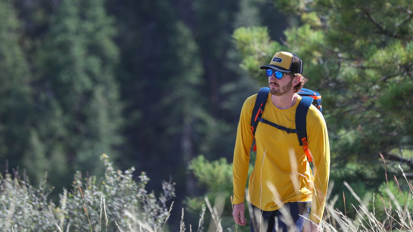 Man in yellow shirt and sunglasses hiking through a forest