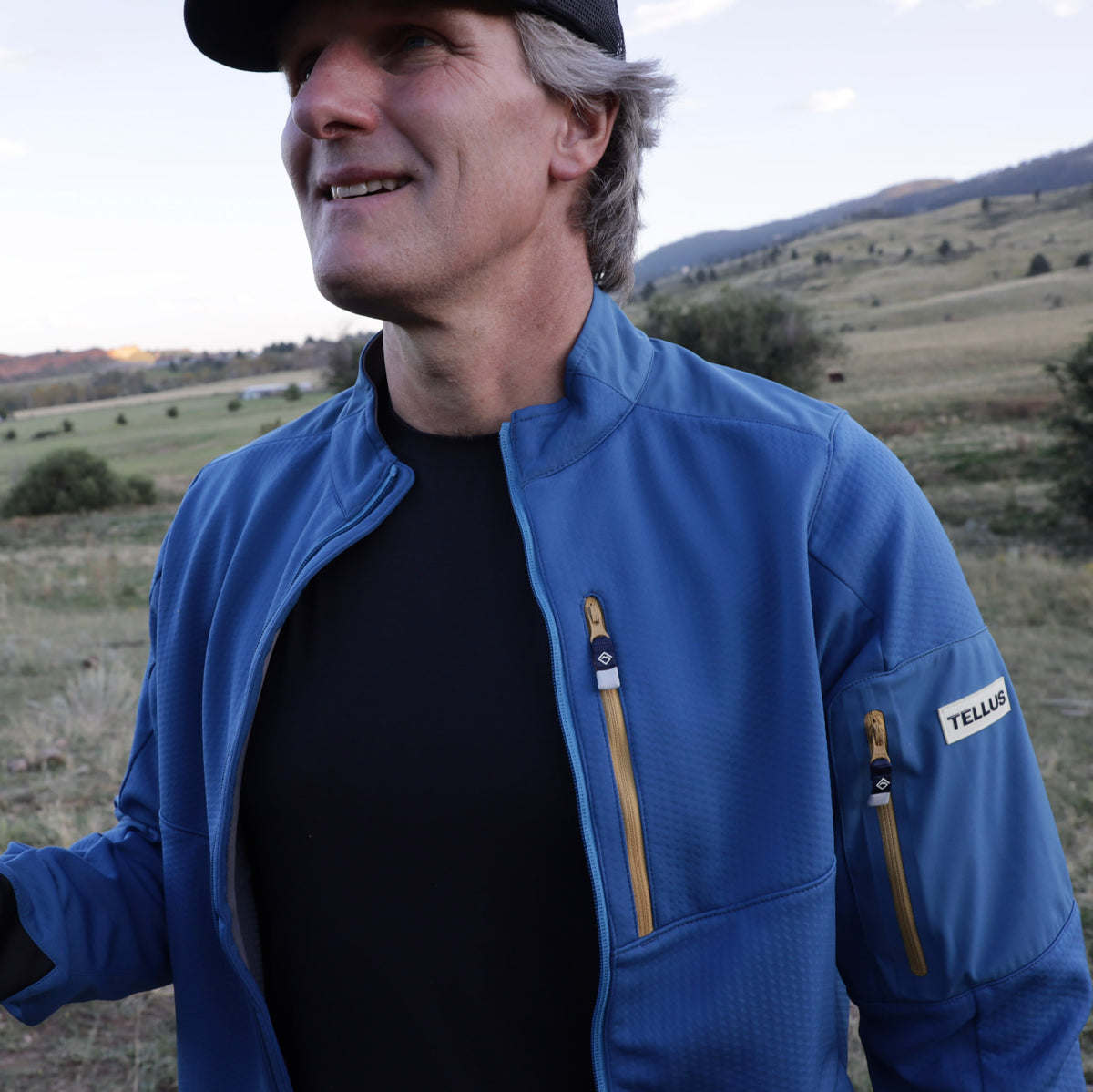 A man wearing a blue Front Range Fleece jacket with hilly background.