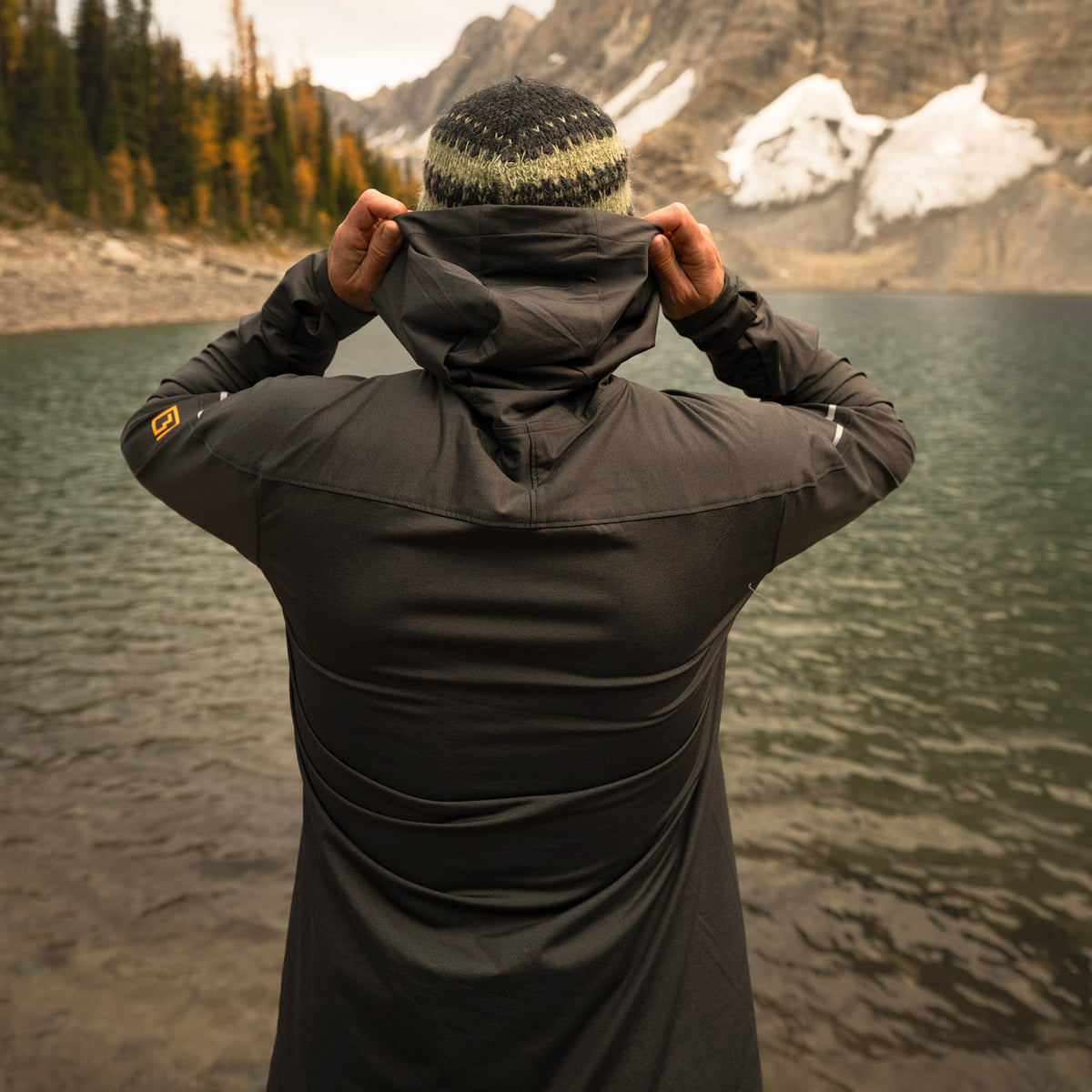 Back of man standing wearing gray Horsetooth Hoodie Quarter Zip with lake, mountains and trees in background.