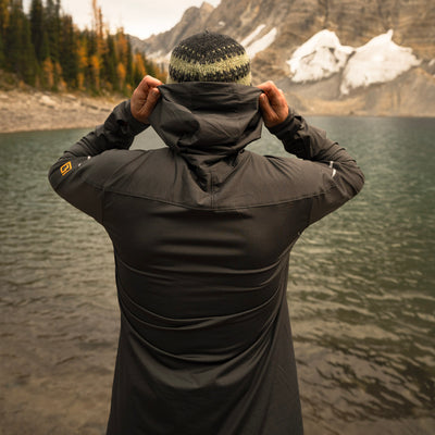 Back of man standing wearing gray Horsetooth Hoodie Quarter Zip with lake, mountains and trees in background.