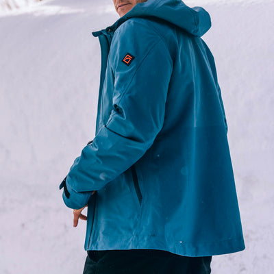 A man wearing a blue Long's Peak Waterproof Rain Shell hooded jacket in a snowy outdoor setting, shown from the side and back.