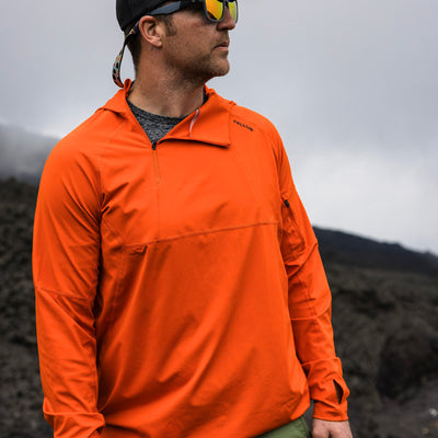 Man wearing orange Satanka Cove Hoodie looking off to the right on a  hilltop with misty, cloudy background