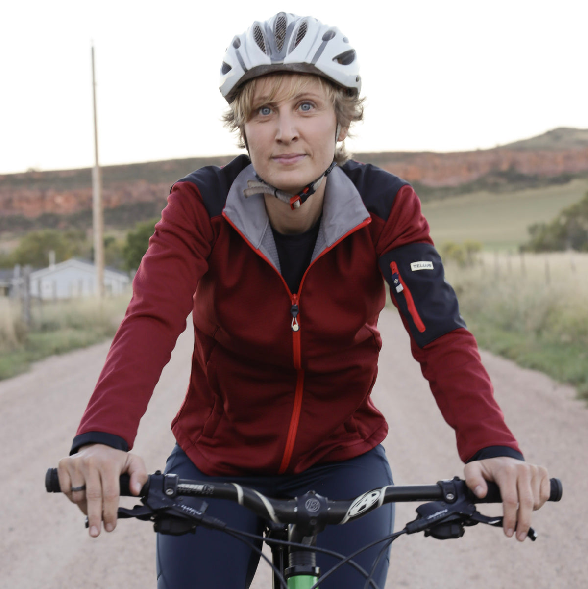 Woman on bicycle wearing orange Front Range Fleece with white helmet in a desert background.