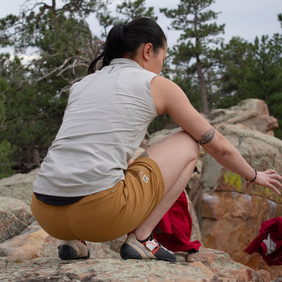 Woman crouching wearing gray Satanka Cove Tank and bistre Trail Ridge Trek Shorts showing back of tank and back of shorts